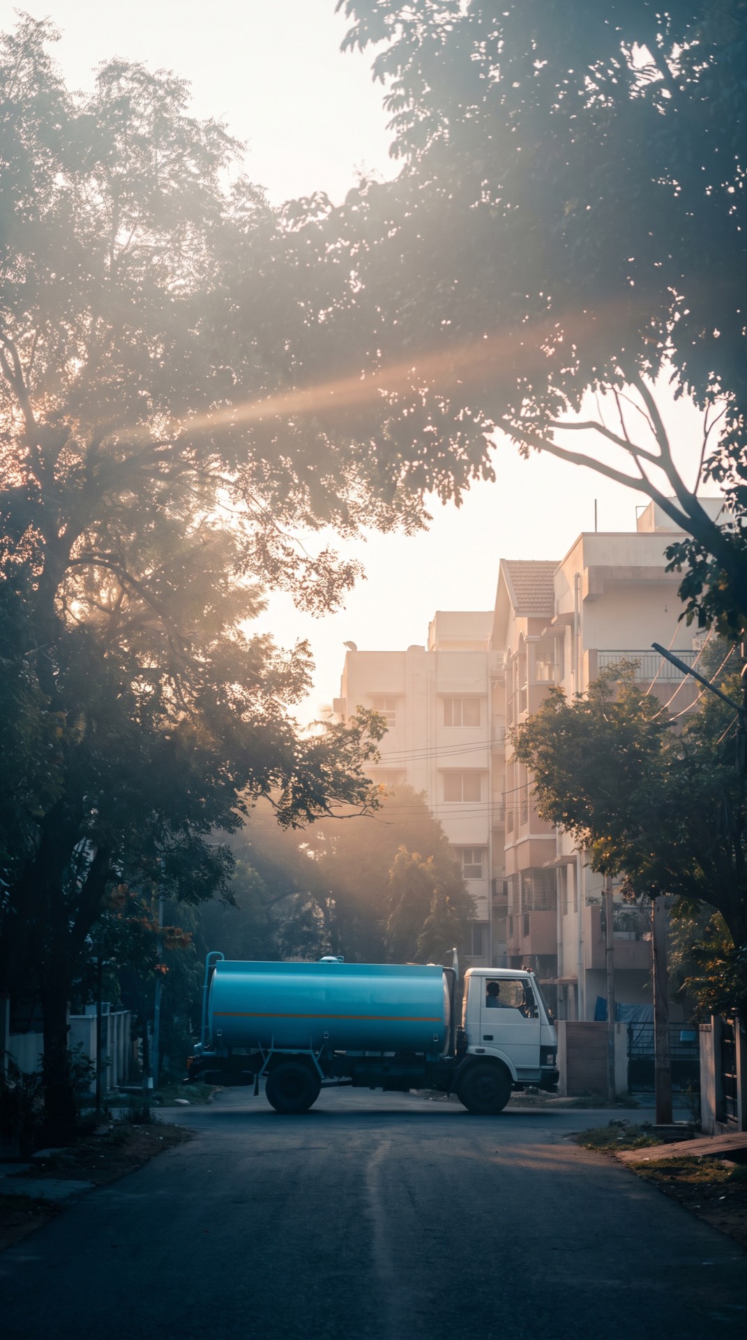 A NeerGo water tanker driving down a tree-lined street at sunrise.